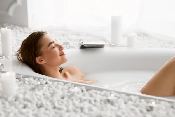 Wanita cantik sedang bersantai di bak mandi susu dengan mata tertutup — Stok Foto