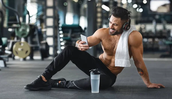 Hombre musculoso usando el teléfono celular en el gimnasio, espacio libre —  Fotos de Stock