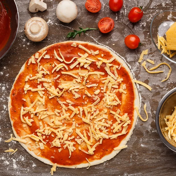 Βάση πίτσας με τριμμένο τυρί και συστατικά γύρω από — Φωτογραφία Αρχείου