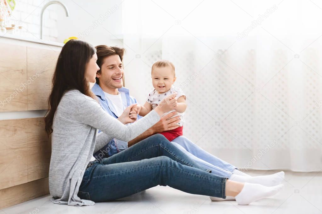 Adorable baby with parents sitting on floor at kitchen