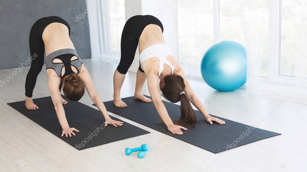 Fit attractive women stretching in Revolved Downward Facing Dog exercise