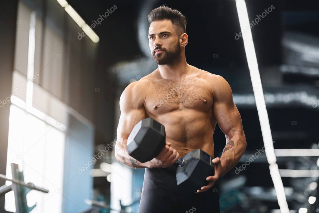 Muscular athlete with naked torso exercising with dumbbell in gym