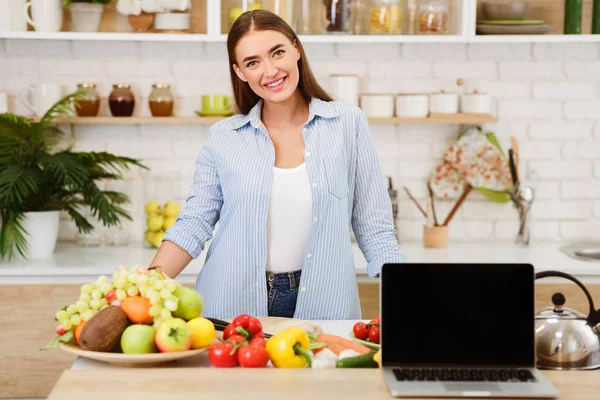 Mujer cocina ensalada mostrando portátil con pantalla en blanco — Foto de Stock