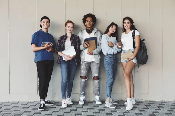 Happy College studenter poserar med att studera personal på Campus Wall — Stockfoto