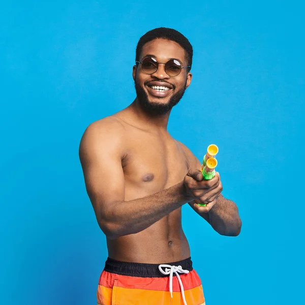 Hombre negro positivo con pistola de agua disparando a la cámara —  Fotos de Stock