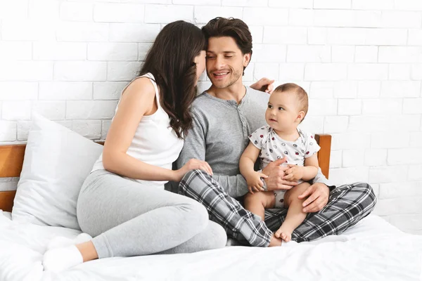 Szczęśliwa młoda rodzina siedzi na łóżku razem w sypialni — Zdjęcie stockowe