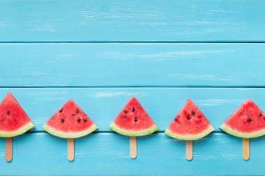 Ahşap çubuklar üzerinde dilimlenmiş karpuz, mavi arka plan.