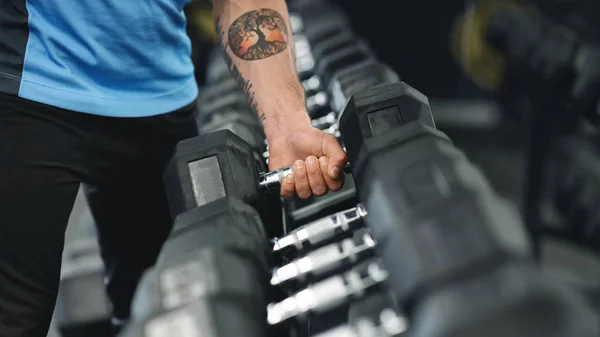 Мышечная мужская рука поднимает тяжелый гантель с вешалки с оборудованием — стоковое фото