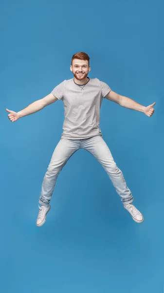 Jovem millennial cara pulando no ar, demonstrando polegares para cima gesto — Fotografia de Stock