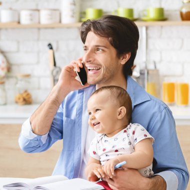 Genç adam ev telefonunda konuşuyor ve bebeğe bakıyor.