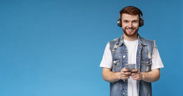 Glimlachend jong man luisteren naar muziek en het houden van mobiele telefoon op de achtergrond — Stockfoto