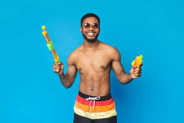 Homem africano alegre em roupa de banho segurando duas armas de água — Fotografia de Stock