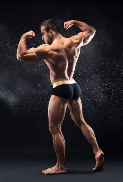 Jovem muscular homem de pé no duplo bíceps pose — Fotografia de Stock