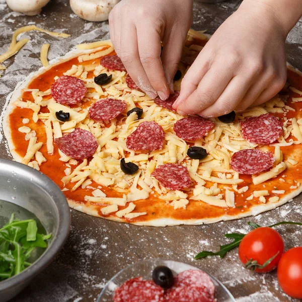 Frau würzt Pizza mit Salami und dekoriert sie mit verschiedenen Zutaten — Stockfoto