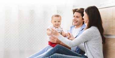 Genç ebeveynler bebekle oynuyor, mutfakta yerde oturuyor.