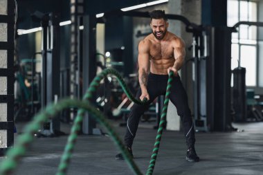 Çıplak kaslı adam spor salonunda savaş halatları ile egzersiz