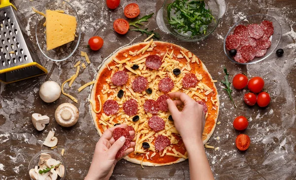 Pizza-Kunst. Frau würzt Pizza mit Salami und Oliven — Stockfoto