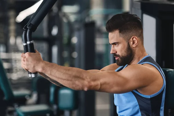 Focused athlete exercising on training machine at gym