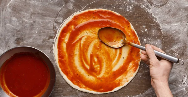 Человек, распространяющий томатный соус на сырой пиццерии — стоковое фото
