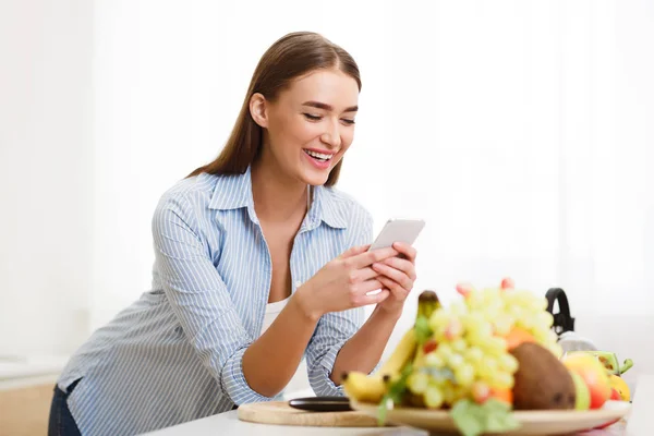 Happy Woman Choosing Recipe On Phone, Cooking In Kitchen