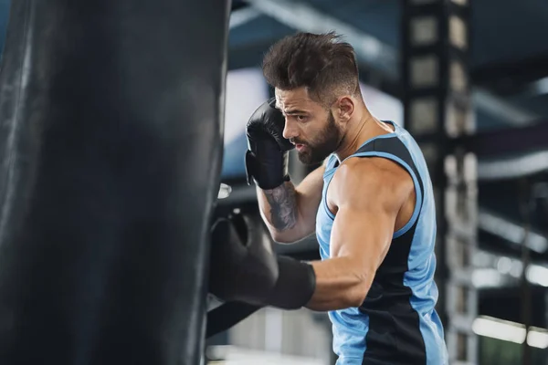 Active guy punching boxing bag at gym