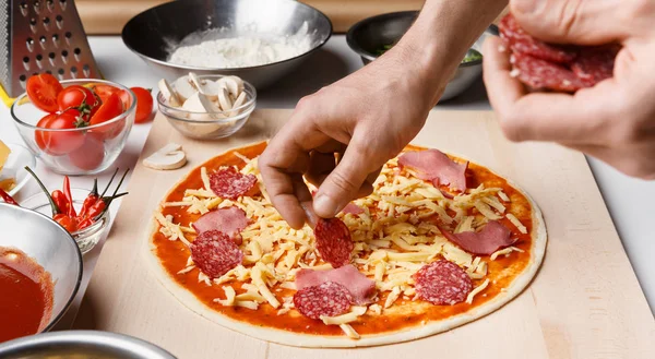 Koch beim Pizzakochen. Hände legen Salami auf Pizzaboden — Stockfoto