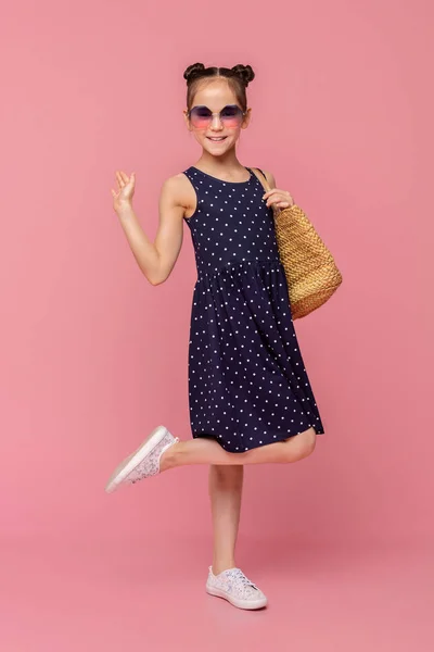 Menina adorável em vestido de verão e óculos de sol andando com saco de vime — Fotografia de Stock