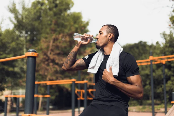 Homem desportivo que bebe a água após o treino na terra dos esportes — Fotografia de Stock