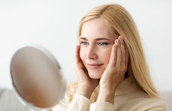 Reife Frau blickt in Spiegel und berührt Gesicht — Stockfoto