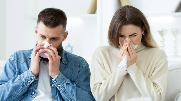 Flu Concept. Couple Blowing Noses In Tissues At Home
