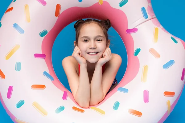 Милая маленькая девочка смотрит через надувное кольцо в форме пончика и улыбается — стоковое фото