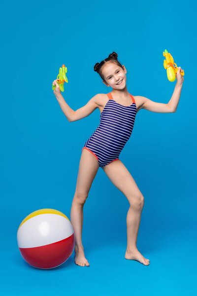 Cute girl playing with water guns and inflatable beach ball