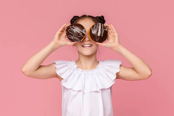 Weinig glimlachend meisje dat haar ogen bedekt met chocolade donuts — Stockfoto