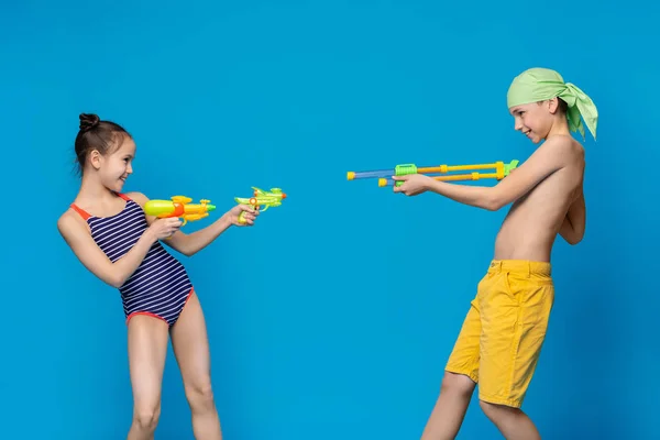 Irmãozinho e irmã atirando uns nos outros com armas de água — Fotografia de Stock