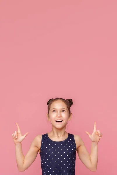Cheerful little girl pointing upwards at free space