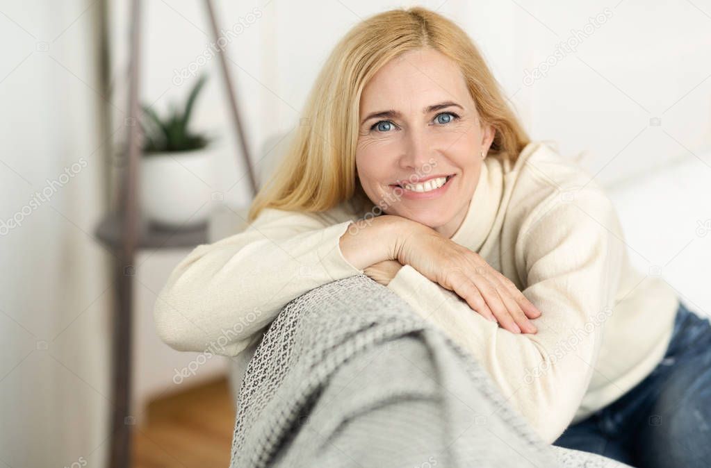 Lovely Middle-Aged Woman With Beaming Smile Sitting On Sofa