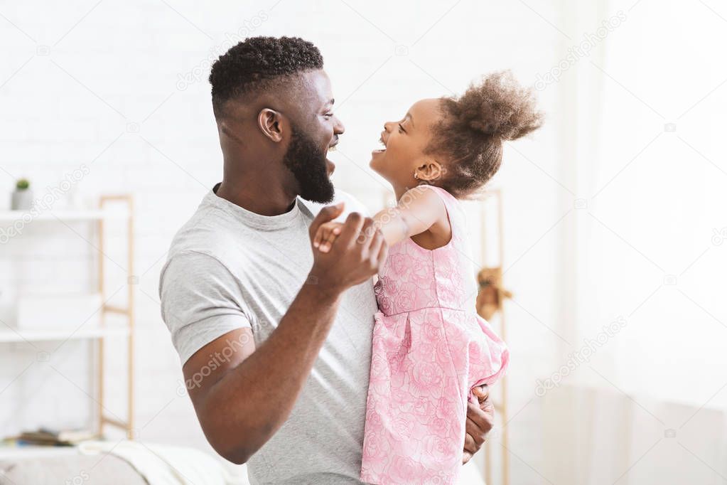 Cheerful black man dancing with his little daughter
