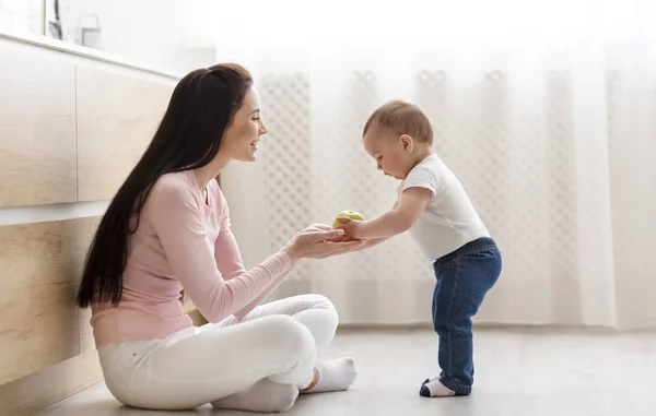 Mãe dando maçã fresca para o bebê, sentado no chão na cozinha — Fotografia de Stock