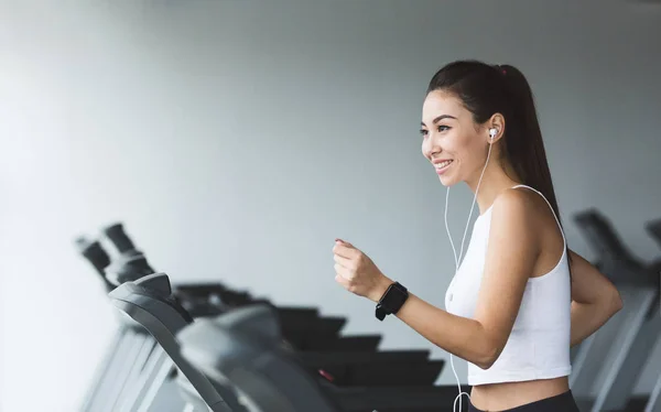 Fittes Mädchen läuft auf Laufband und hört Musik im Fitnessstudio — Stockfoto