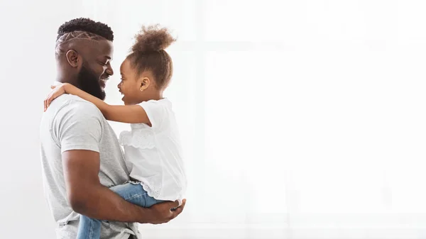 Negro hombre abrazando su lindo poco hija cerca ventana —  Fotos de Stock