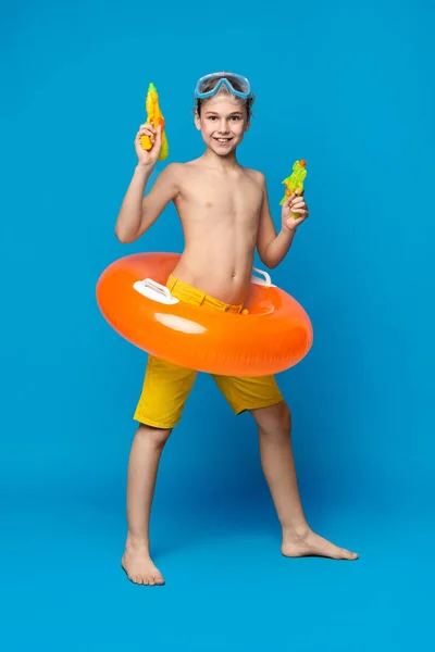 Хлопчик-підліток у купальнику, що стоїть з водяними гарматами — стокове фото