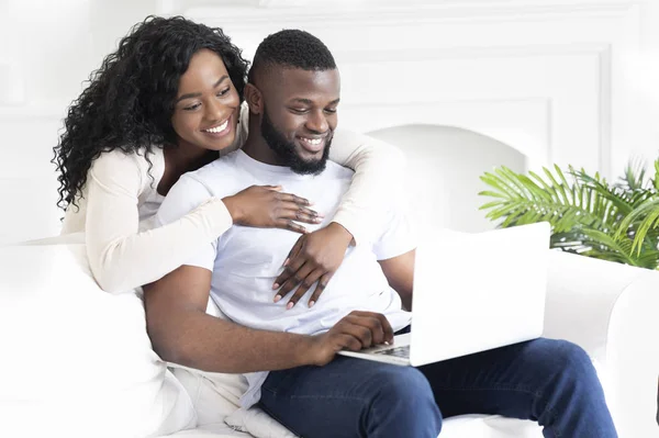 Black guy working at home on laptop, loving wife embracing him