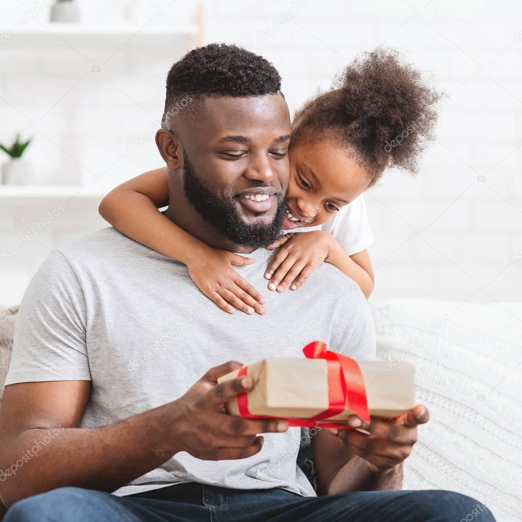 Cute african child girl hugging dad and giving him gift