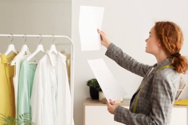 Genç tasarımcı kontrol ve kağıtlar üzerinde çizimler karşılaştırma