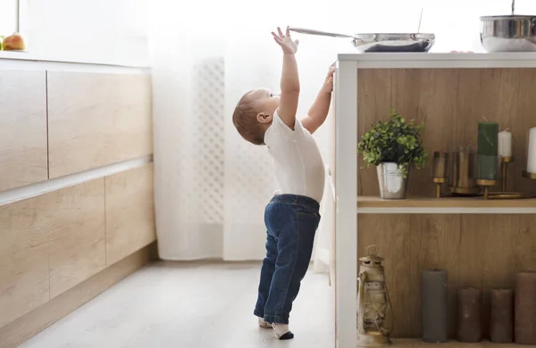 Безпека дитини вдома концепція - малюк досягає сковороди на плиті на кухні — стокове фото