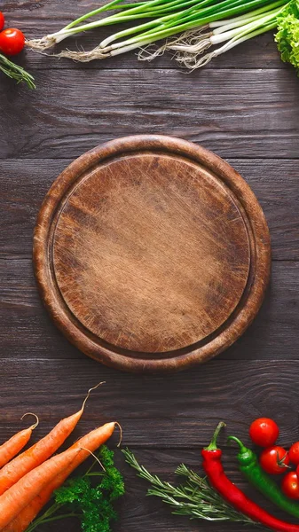 Wooden platter surrounded by fresh vegetables on rustic table