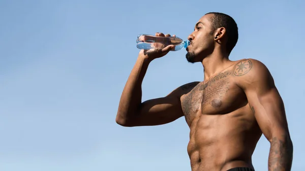Muskulární Afro muž pitná voda po cvičení proti modrému nebi — Stock fotografie