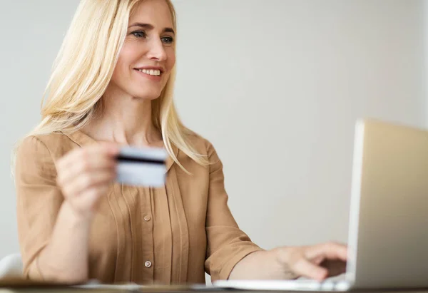 Зріла жінка тримає кредитну картку і купує онлайн — стокове фото