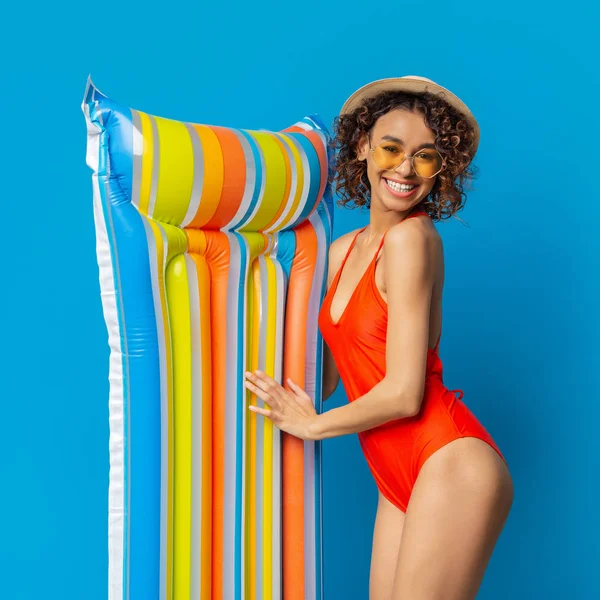 Senhora africana feliz em roupa de banho sorrindo com colchão de natação colorido — Fotografia de Stock