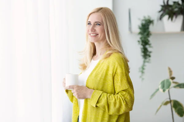 Café Morning. Madura mujer celebración taza cerca de la ventana — Foto de Stock